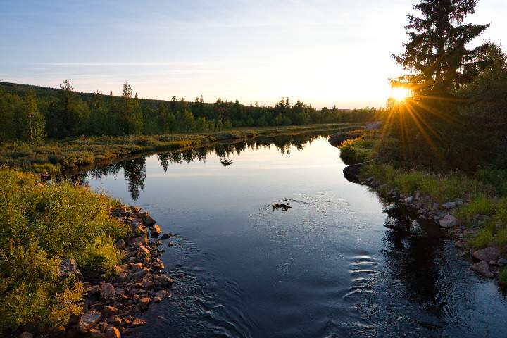 Ein kleiner Fluss windet sich durch die Wildnis in Schweden vor der untergehenden Sonne kurz vor dem Björnlandet Nationalpark