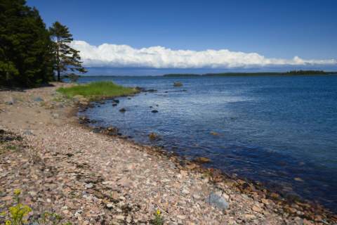 Ein Ufer mir groben Kieselsteinen im Bottensee Nationalpark auf der Insel Iso-Enskeri. Im Hintergrund eine Wolkenfront über weiteren Inseln.