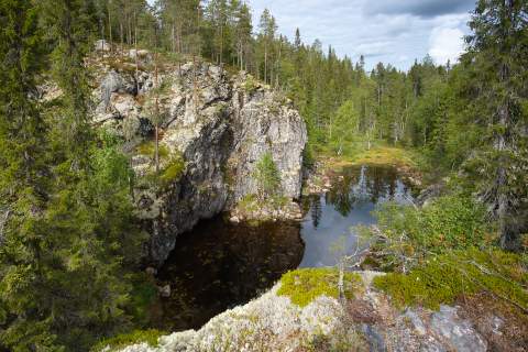 Steile Felsen säumen das Ufer eines kleinen Sees im Hiidenportti Nationalpark. Wo immer sich Bäume einen Untergrund finden wächst ein dichter Nadelwald.