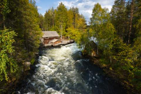 Historische Myllykoski-Mühle am Wildbach im Oulanka-Nationalpark in Finnland, umgeben von Herbstwald und rauschendem Wasser.