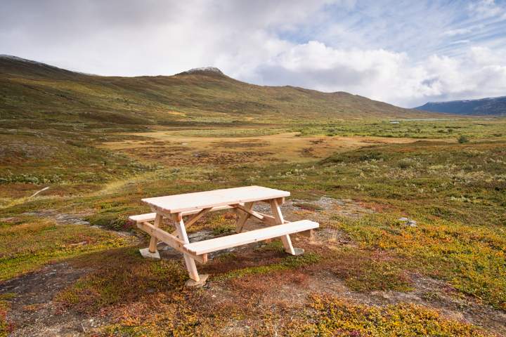 Ein Tisch mit Bänken steht auf einer Anhöhe in Darreluopal. Die Weite Hügellandschaft des Padjelanta Nationalparks liegt dahinter.