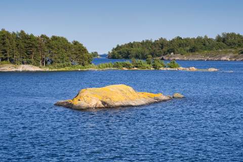 Ein Felsen im Meer vor bewaldeten Inseln im Schärenmeer Nationalpark, auch Archipelago oder Saaristomeren Nationalpark genannt