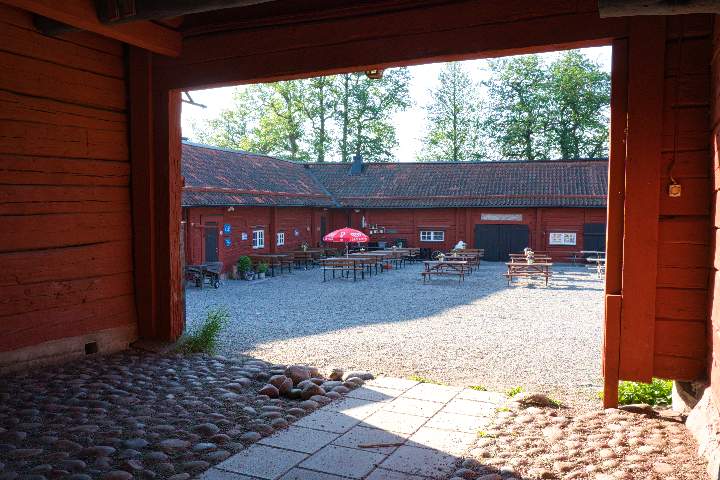 Durch eine Tor des historischen Gehöftes blickt man in den Innenhof mit Tischen und Bänken eines Cafés